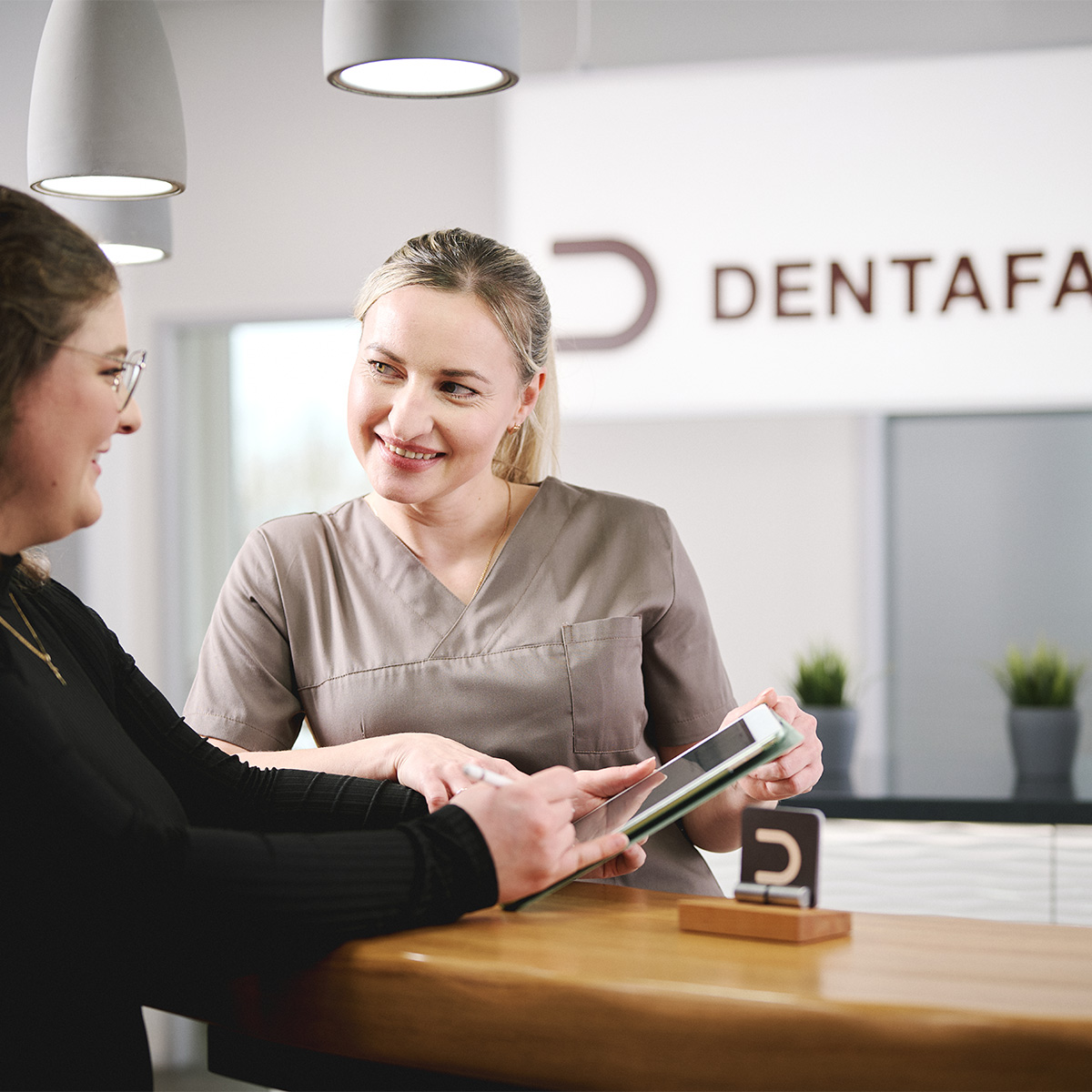 Freundliches Zahnarztteam der Dentafamily Margetshöchheim erklärt Behandlungsablauf auf Tablet.